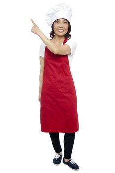 Beautiful female chef pointing at the copy space. Full length shot