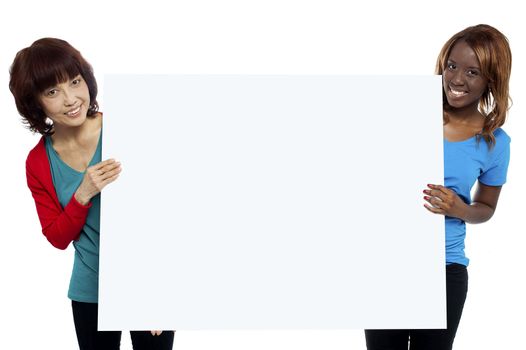 Two ethnic female models presenting whiteboard isolated against white background