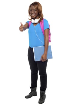 Trendy confident college showing thumbs up to camera. Enjoying music through headphones