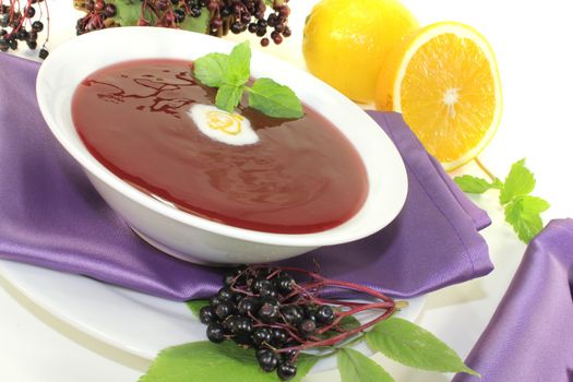 healthy elderberry soup with blobs of cream and mint on a bright background