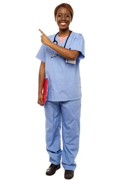 Female doctor pointing at copy space, holding clipboard. Full length portrait