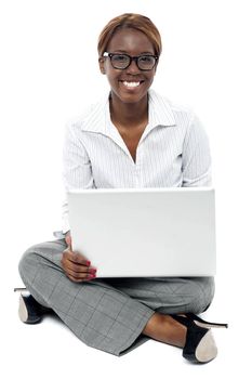 Corporate lady seated on floor working on laptop. Looking at camera and smiling
