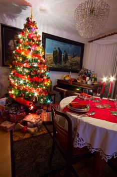Cozy room with presents under decorated Christmas tree, old piano and table ready for Christmas dinner