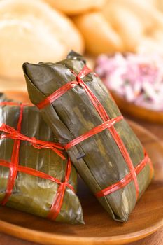 Peruvian tamales wrapped in banana leaves, in which they are cooked. Inside is a a corn-based dough with meat. Tamales in Peru are traditionally consumed as breakfast on Sundays accompanied by buns, limes and salsa criolla (onion salad) (Selective Focus, Focus on the front of the standing tamale)