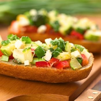 Baked vegetarian open sandwich (red bell pepper, zucchini, scallion and cheese on bun) on wooden board (Selective Focus, Focus one third into the topping on the sandwich) 