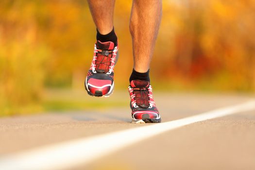 Athlete running shoes close-up. Man runner jogging outdoors in fall / autumn color. Closeup of male running shoes in action.
