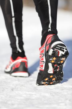 Running shoes in snow with grip soles or traction cleats with metal spikes for anti slip grip when walking or running. Man winter running in snow.