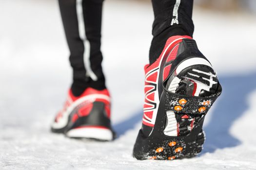 Running shoes in snow with grip soles or traction cleats with metal spikes for anti slip grip when walking or running. Man winter running in snow.