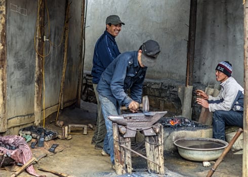 Men beating the metal on anvil while fire burns.