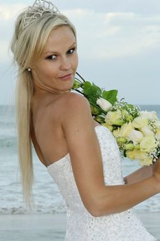 Gorgeous blond bride with bouquet of flowers at the beach