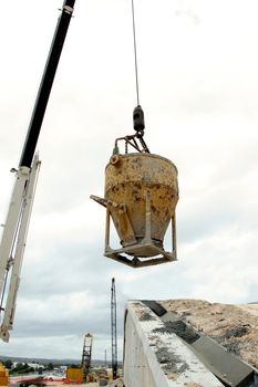 Steel bucket filled with concrete being lifted by a crane on a construction site
