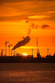 Industrial background, cranes, pollution and   orange sunset - vertical