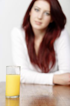 Glass of Orange juice with a female sitting in the background leaning on a table