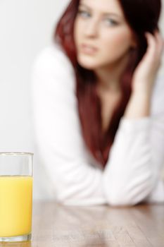 Glass of Orange juice with a female sitting in the background leaning on a table