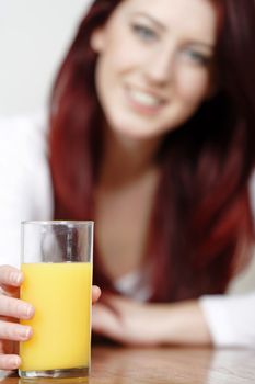 Glass of Orange juice with a female sitting in the background leaning on a table