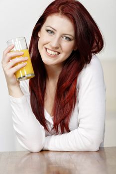 Smiling happy young woman leaning on a wooden table with a fresh glass of Orange juice during breakfast.