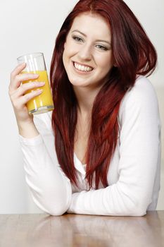 Smiling happy young woman leaning on a wooden table with a fresh glass of Orange juice during breakfast.