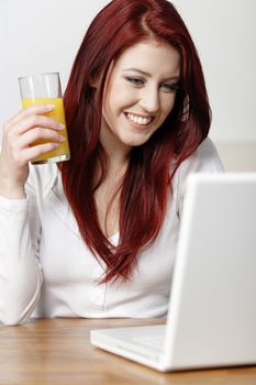 Beautiful young woman using a laptop at home with a fresh glass of Orange juice.