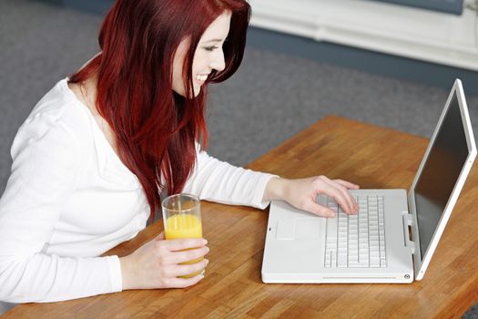 Beautiful young woman using a laptop at home with a fresh glass of Orange juice.