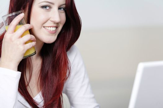 Beautiful young woman using a laptop at home with a fresh glass of Orange juice.
