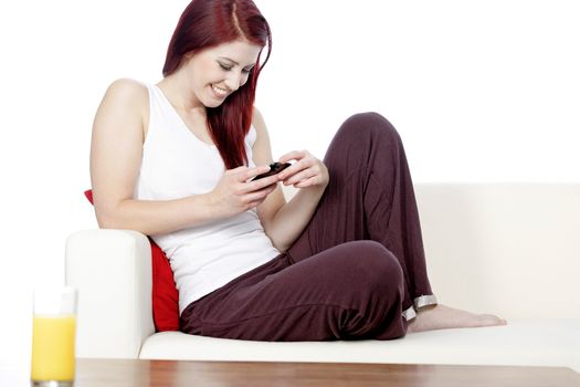 happy young woman sat on her white sofa at home smiling at text messages on her phone