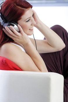 Happy smiling young woman listening to music at home on headphones