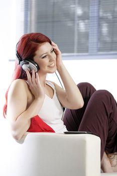 Happy smiling young woman listening to music at home on headphones