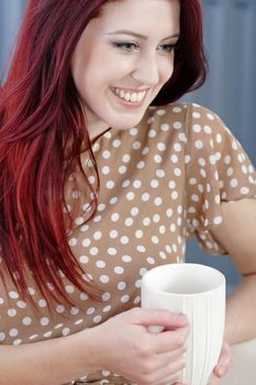 Happy young woman sitting on a sofa at home enjoying a coffee break.