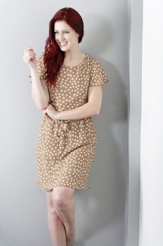 Beautiful happy young woman in a summer dress leaning against a wall.