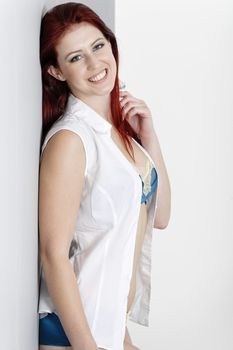 Smiling beautiful woman in blue underwear and white shirt leaning against a wall