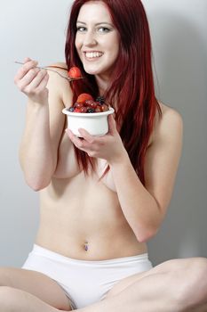 Beautiful young woman sat against a wall enjoying a bowl of fresh fruit