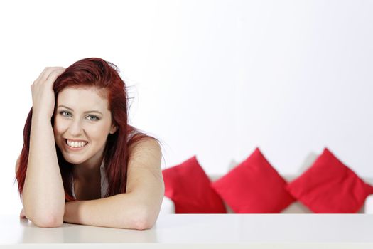 Beautiful young woman leaning on a table at home with a sofa in the background.