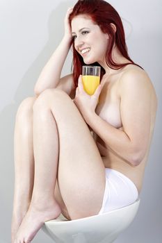 beautiful young woman sat on a stool with a glass of fresh Orange juice in her underwear.