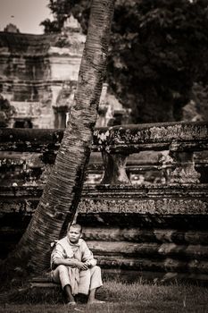 SIEM REAP, CAMBODIA - CIRCA JUNE 2012: Unidentified buddhist monk sitting on the edge of the reflection pool circa June 2012 in Angkor Wat, Cambodia The monastery is still use as part of worship sacred place.