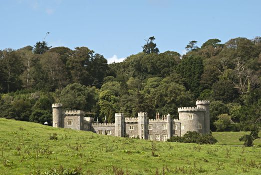 A Nineteenth Century Country House built in the Style of a castle with woodland under a blue sky