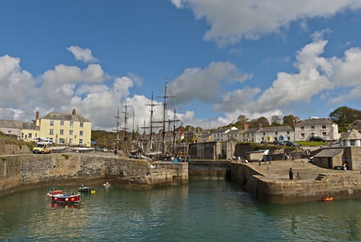 The Historic Harbour of Charlestown in Cornwall under a blue sky with tall ships