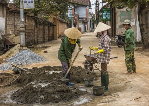 Vietnam Duong Lam . Two women construction workers handle shovel and buckets of water while man looks on.