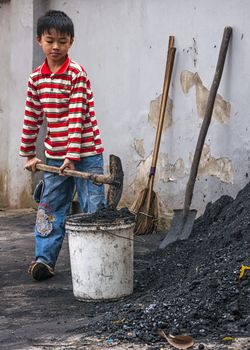 Vietnam Duong Lam. Kid with colorful shirt uses shovel to put black coal in white bucket.