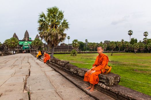 SIEM REAP, CAMBODIA - CIRCA JUNE 2012: Unidentified buddhist monk sits on the edge of the causeway/walkway circa June 2012 in Angkor Wat, Cambodia The monastery is still use as part of worship sacred place.