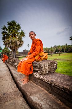 SIEM REAP, CAMBODIA - CIRCA JUNE 2012: Unidentified buddhist monk sits on the edge of the causeway/walkway circa June 2012 in Angkor Wat, Cambodia The monastery is still use as part of worship sacred place.
