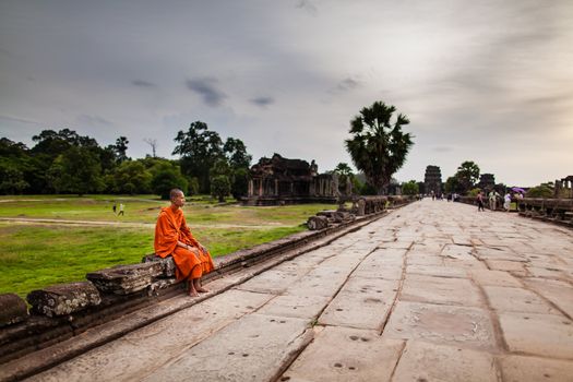 SIEM REAP, CAMBODIA - CIRCA JUNE 2012: Unidentified buddhist monk sits on the edge of the causeway/walkway circa June 2012 in Angkor Wat, Cambodia The monastery is still use as part of worship sacred place.