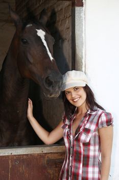 Beautiful smiling brunette woman with her horse in a stable