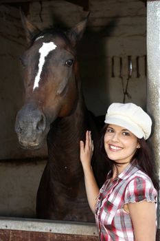 Beautiful smiling brunette woman with her horse in a stable