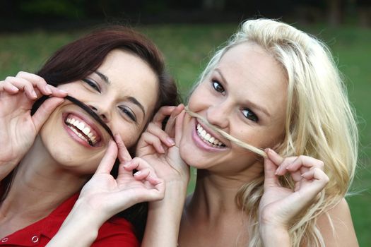 Two beautiful lady friends pretending to have moustaches