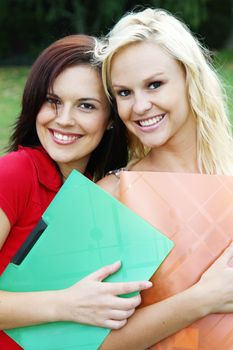 Two lovely young student friends holding folders and standing outdoors