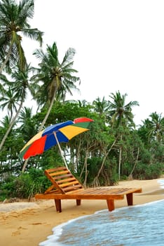 umbrella and lounge chair on the shore of exotic island with palm trees