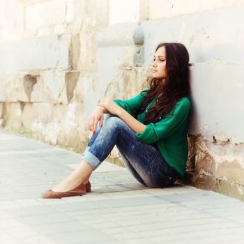 Portrait of beautiful young girl, sitting leaning on an old wall