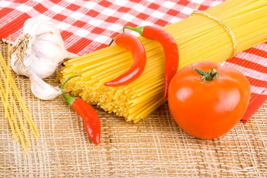 Golden raw dried Italian pasta with other ingredients on kitchen desk.