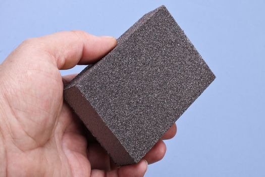 Men`s hand with sanding sponge and blue background