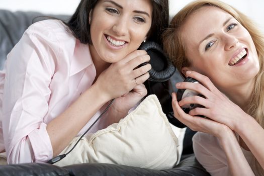 Two young woman listening to music on headphones at home.